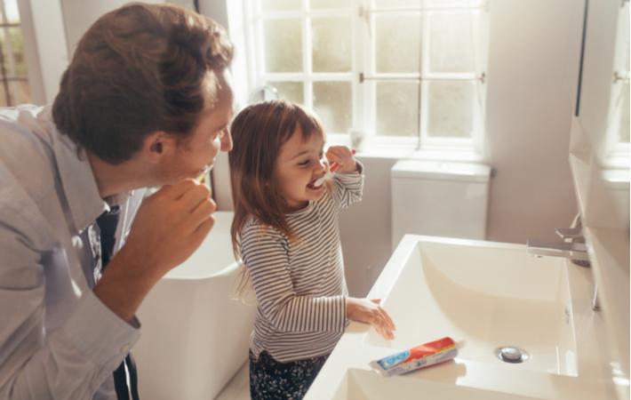 father and daughter brushing teeth together in bathroom