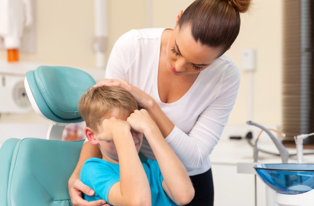 Child crying in the dentist's chair being comforted by his mother