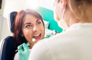 Woman in a dentist's chair smiling up at her dental hygienist wearing rubber gloves and holding dental cleaning tools