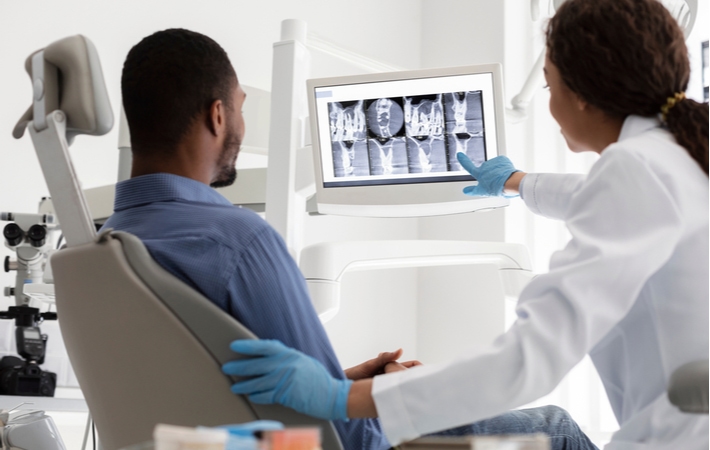 A female dentist and male patient looking at x-ray results on a digital screen at a dental clinic