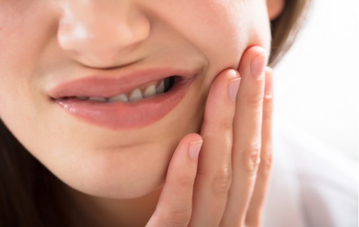 A woman with sensitive teeth holding her cheek in discomfort