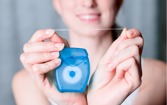 A woman holding out a piece of dental floss to encourage great oral health