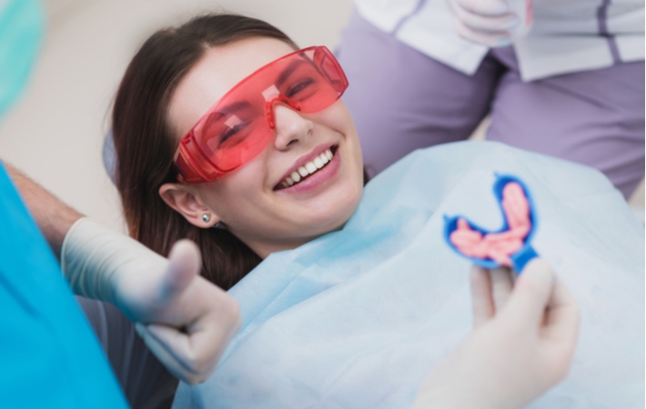 A girl smiling, ready for her dentist to insert a blue mouthguard with fluoride into her mouth at the end of her dental treatment