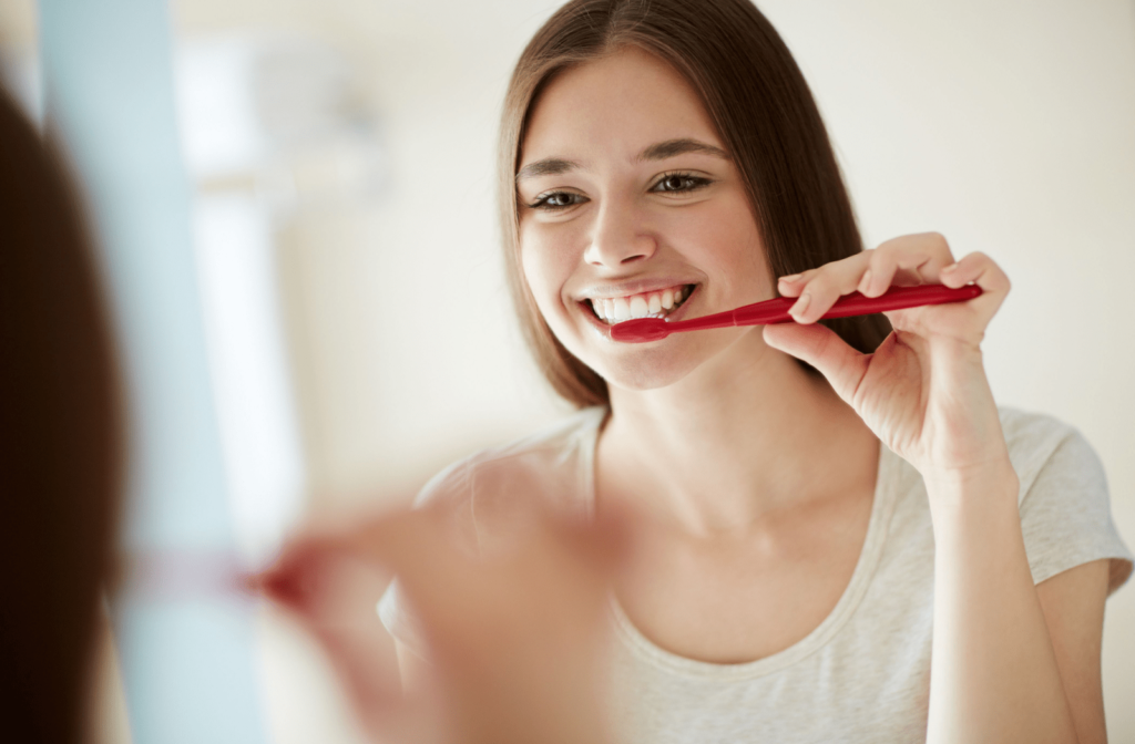 A girl in the mirror brushing her teeth with a soft bristle toothbrush to prevent her sensitive gums from bleeding