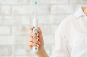 A woman holding up an electric toothbrush in her right hand