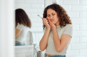 A woman brushing her teeth in her bathroom stops and winces in pain from her teeth