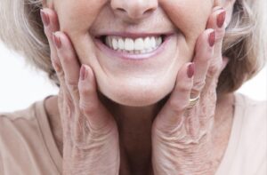 A woman holding the side of her face with both hands and she's smiling
