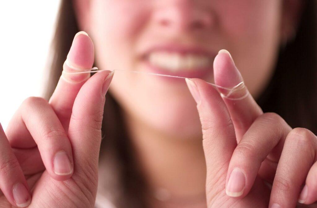 A closeup of a young woman's fingers demonstrates the correct way to hold floss.