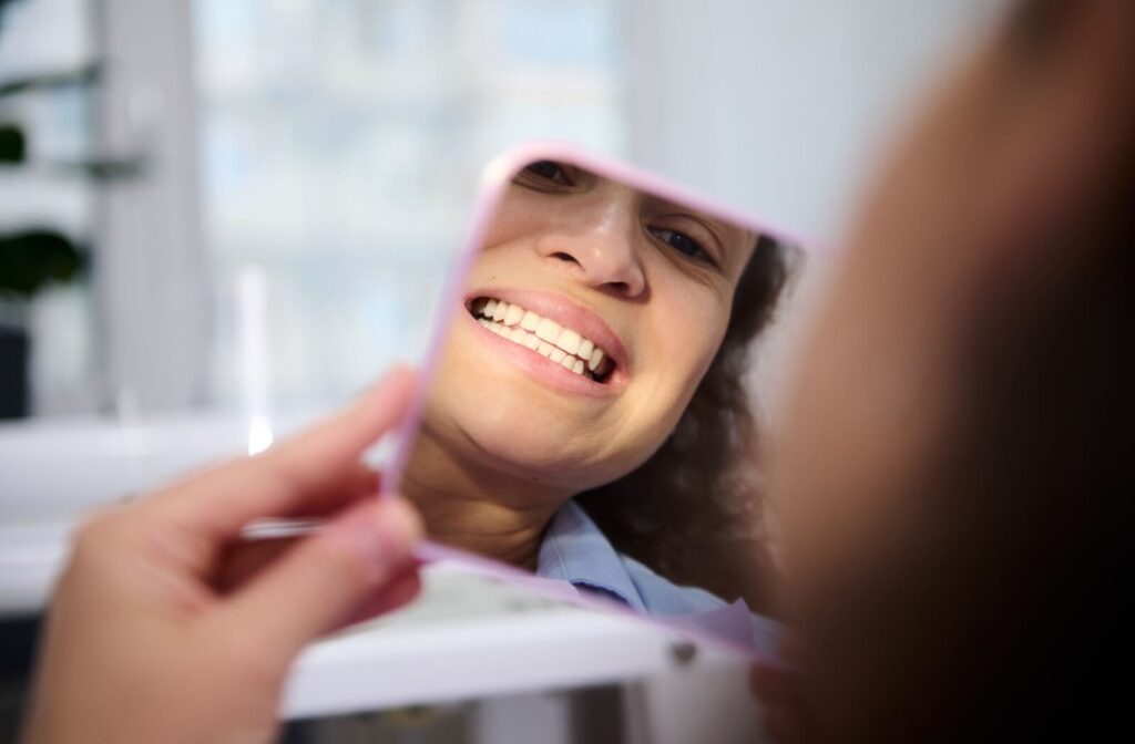 A person examines their teeth in a mirror at a dentist's office after their dental filling.