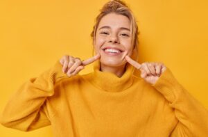 A person happily pointing to their bright, white smile.