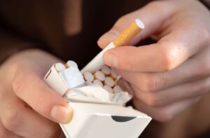 A person's hand slowly pulls a cigarette out of a new pack of cigarettes.