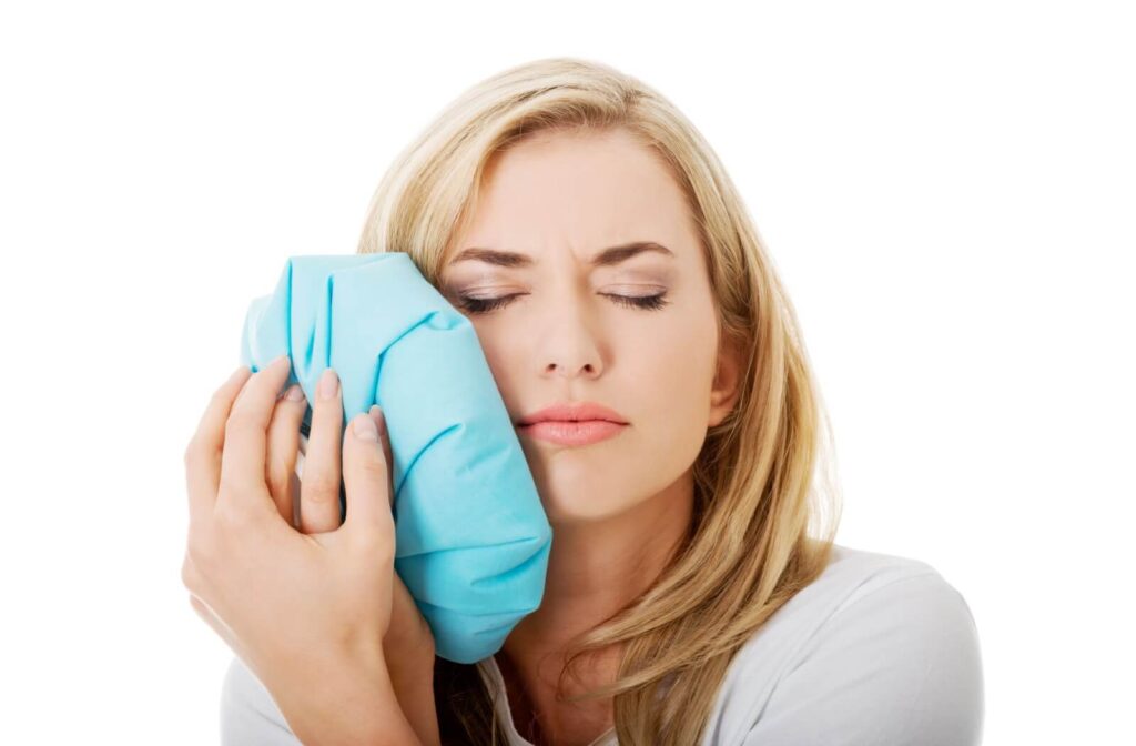 A person recovering from a root canal holds an ice pack to their cheek to help relieve the swelling in their mouth.