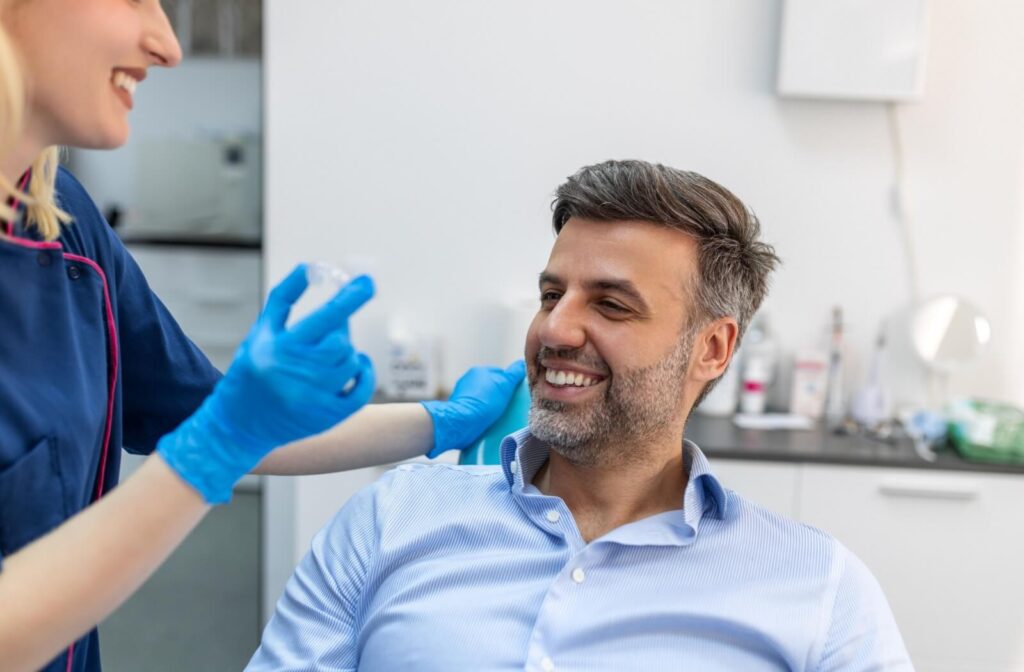 A patient sitting in an exam chair in a bright clinical setting as a dentist starts to place a clear retainer in their mouth